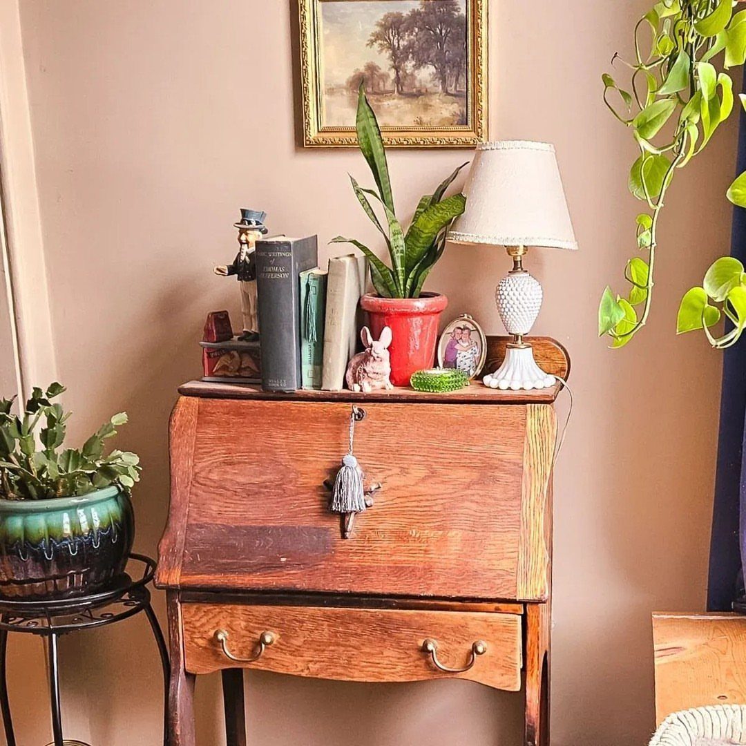 Vintage wooden slant-front secretary desk with a lamp and books on top.