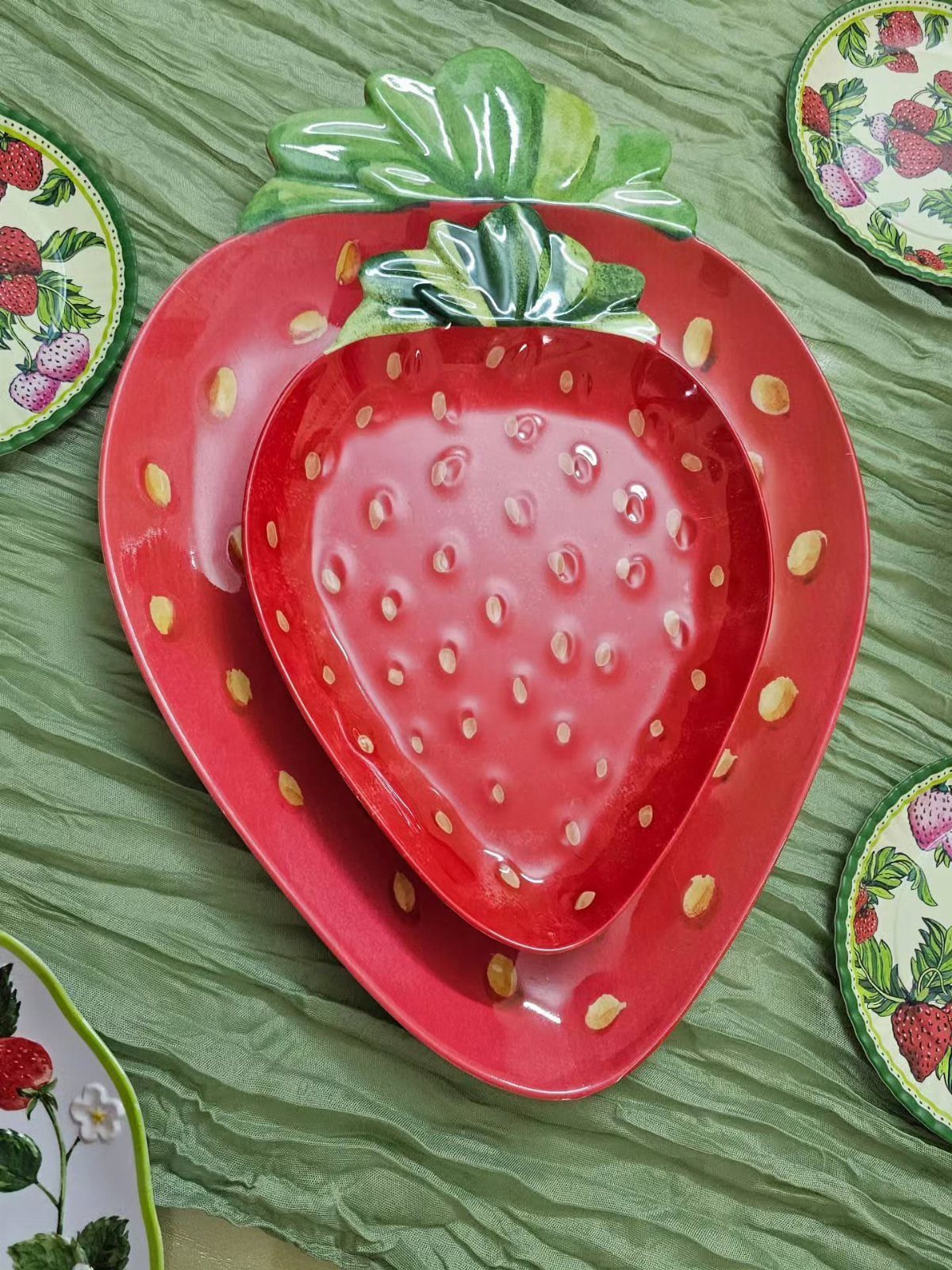 Fruit Shaped Plates in 12 Styles 7 Strawberry shaped red ceramic plate and bowl on a green textured fabric background.