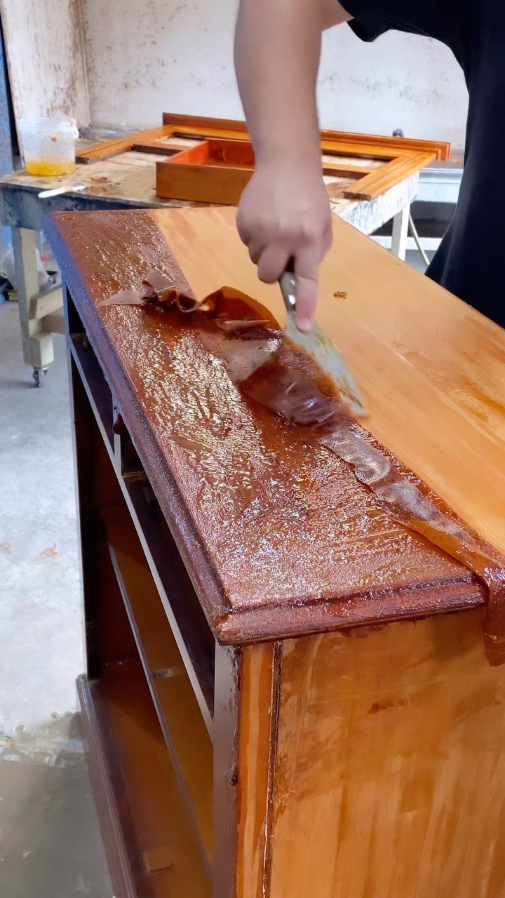 Hand scraping old varnish off a wooden cabinet during a furniture refinishing project