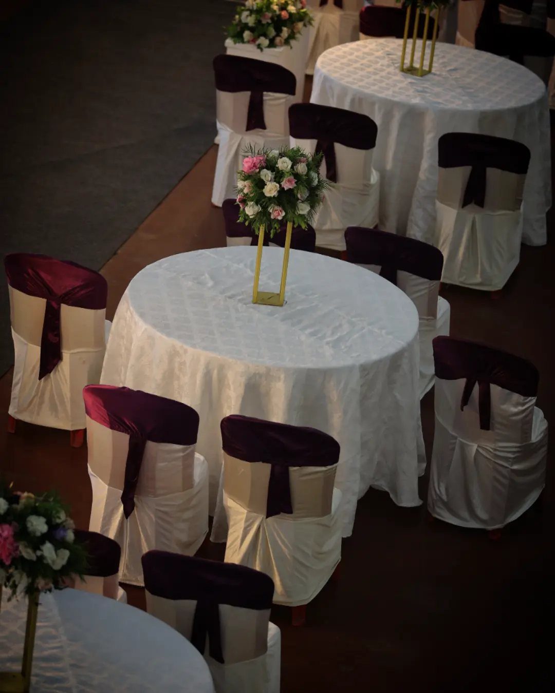 Table Decor for Round Tables: 13 Ideas to Try at Home 9 Round tables with white linens and tall gold floral centerpieces in a banquet hall.