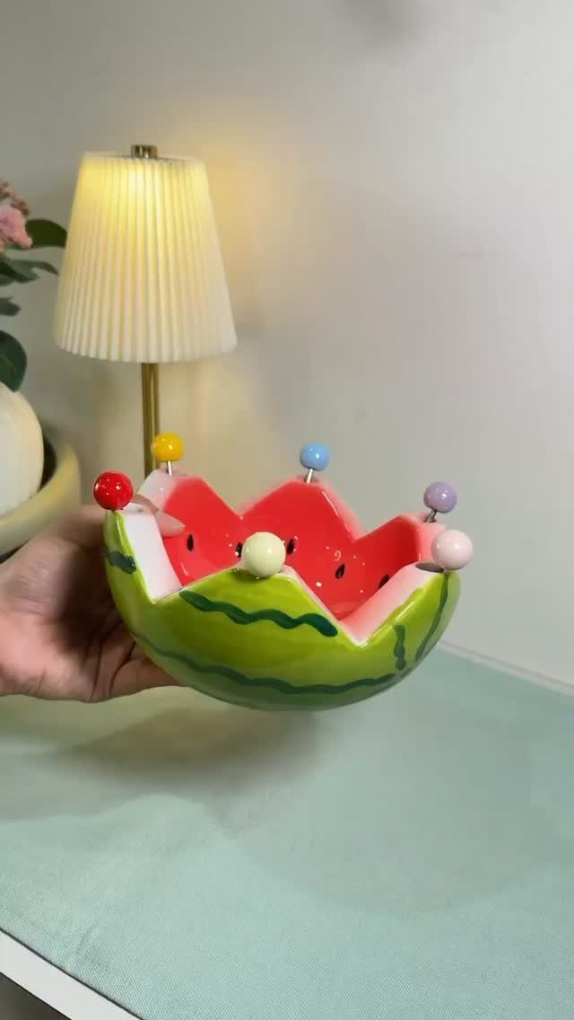 Fruit Shaped Plates in 12 Styles 4 Watermelon shaped ceramic bowl with colorful spheres held by a hand.
