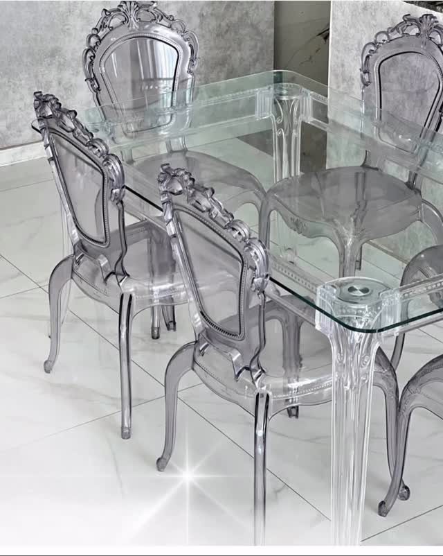 Transparent acrylic dining table and ornate clear chairs on a white tiled floor.