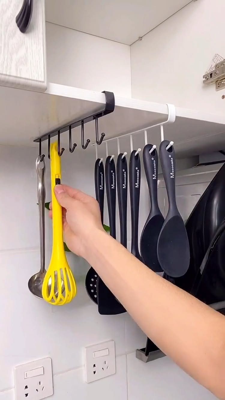 17 Ways to Organize Kitchen Tools (With Photos for Each) 14 Yellow slotted spoon and grey utensils hanging from an under-shelf rack in a kitchen