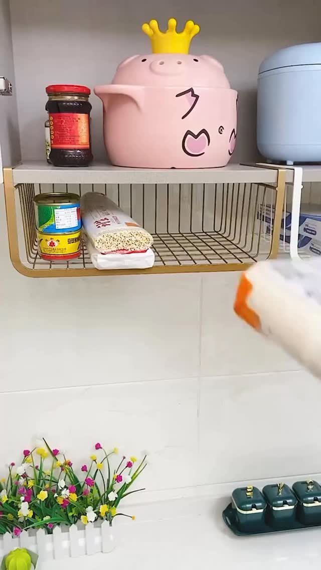 Gold metal undershelf basket holding a jar and noodles beneath a white kitchen shelf.