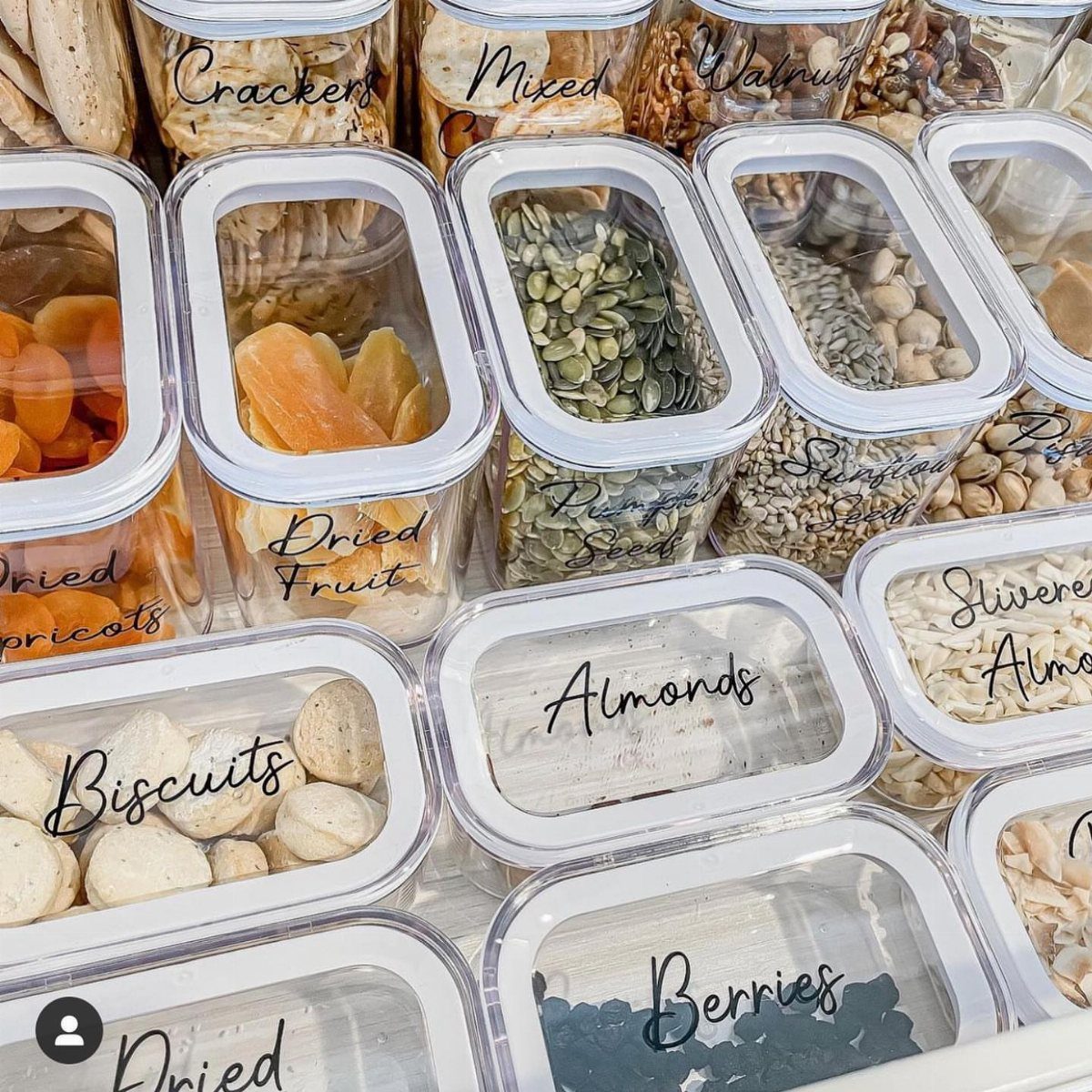 Flat clear plastic containers with labels holding dried fruits and nuts on a shelf.