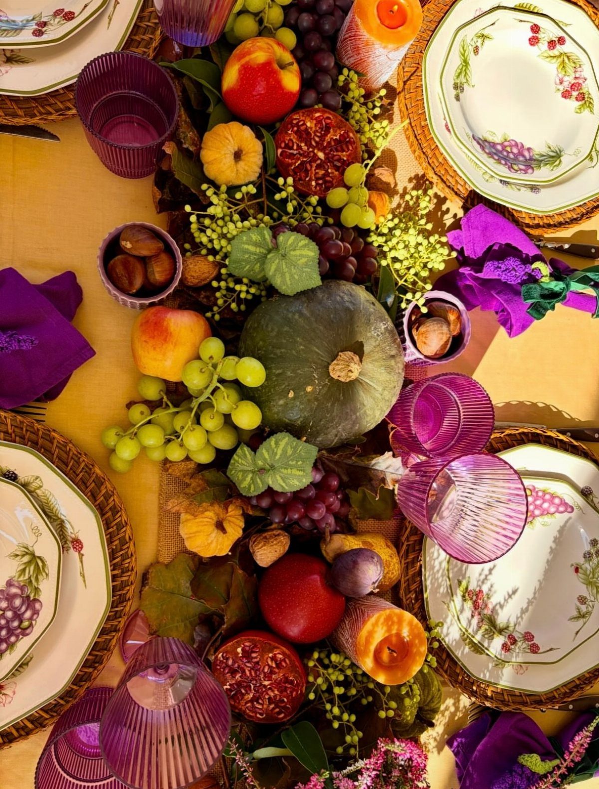 Table Decor for Round Tables: 13 Ideas to Try at Home 13 Autumnal table setting with a centerpiece of pumpkins, grapes, and pomegranates on yellow linen.