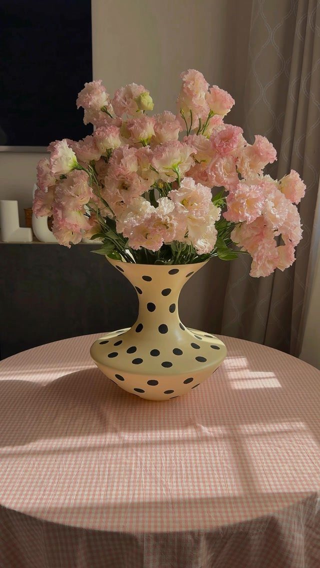 Table Decor for Round Tables: 13 Ideas to Try at Home 2 Pink flowers in a yellow polka dot vase on a round checkered table.