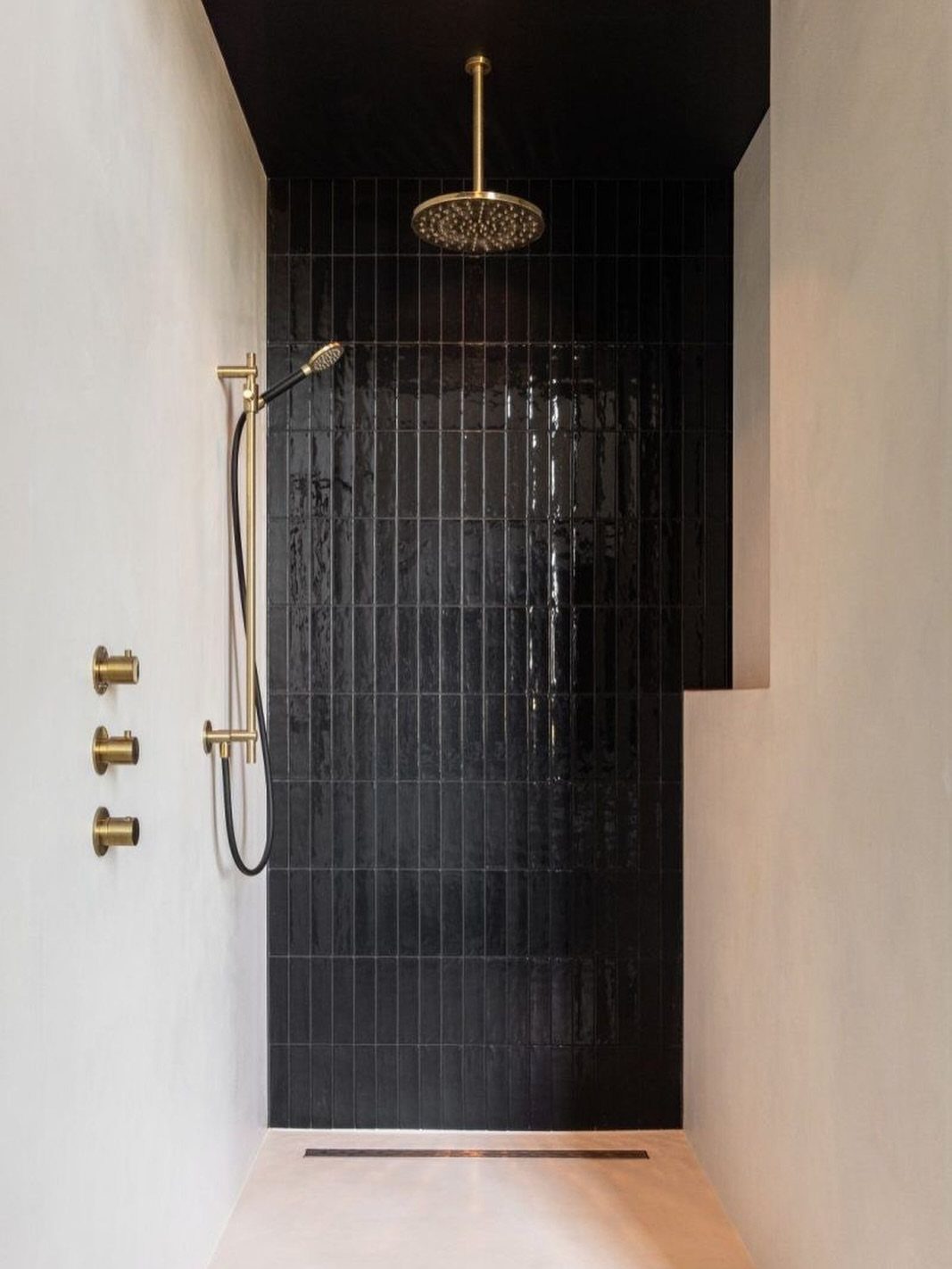 Black Mosaic Tile Bathroom: 14 Designs from Hex to Herringbone 11 Black mosaic tile shower wall with gold fixtures and white surrounding walls.