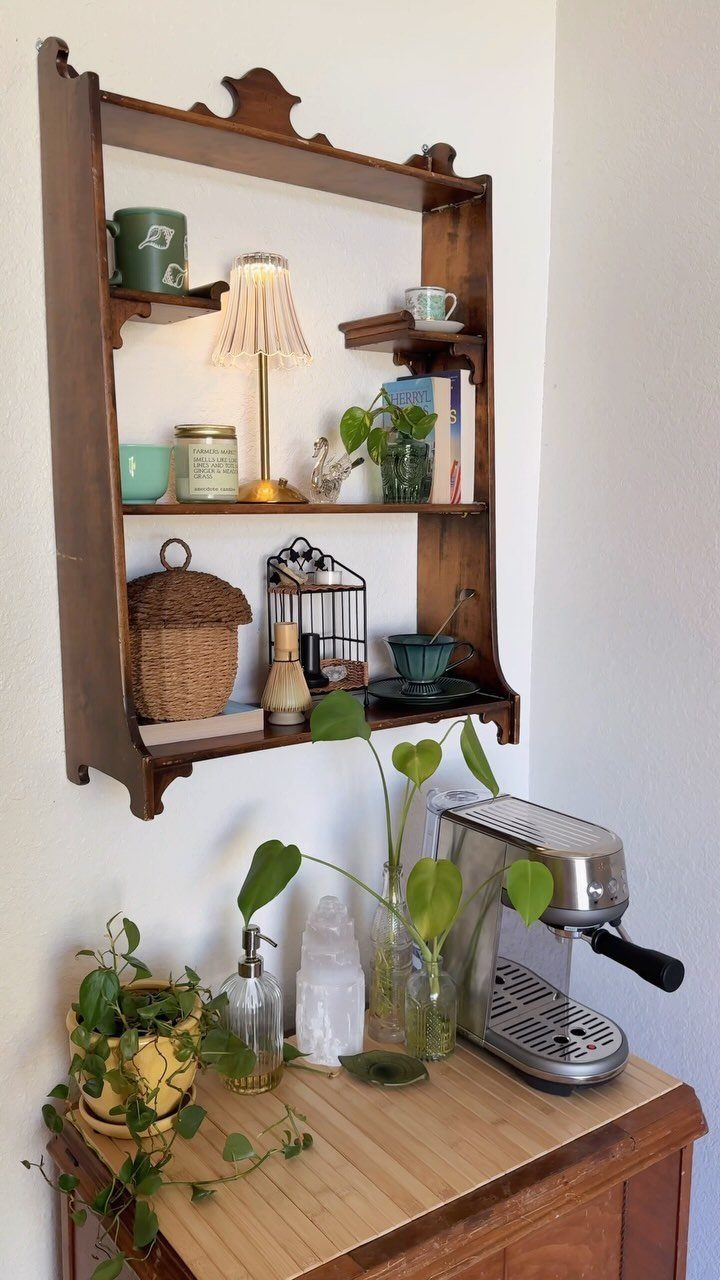 Vintage wooden coffee bar with espresso machine, wall shelving, and green indoor plants.
