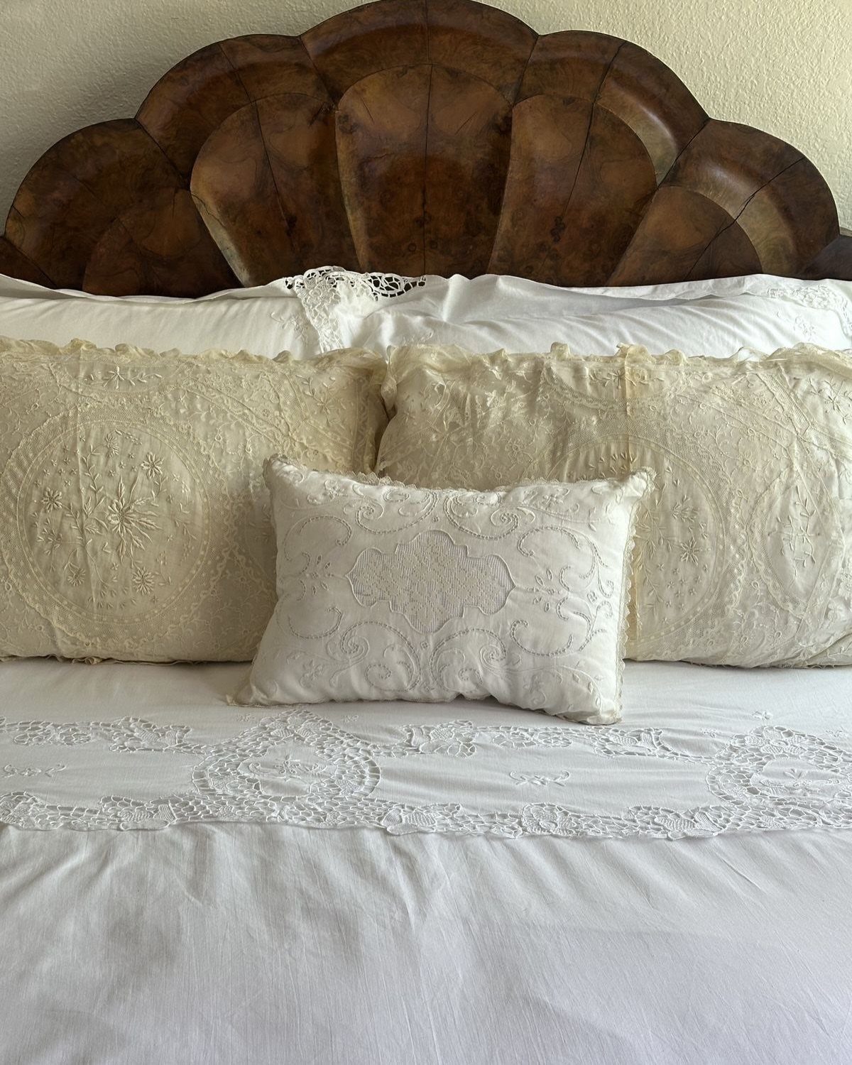 Shell-shaped brown wooden headboard with white lace bedding and cream pillows.