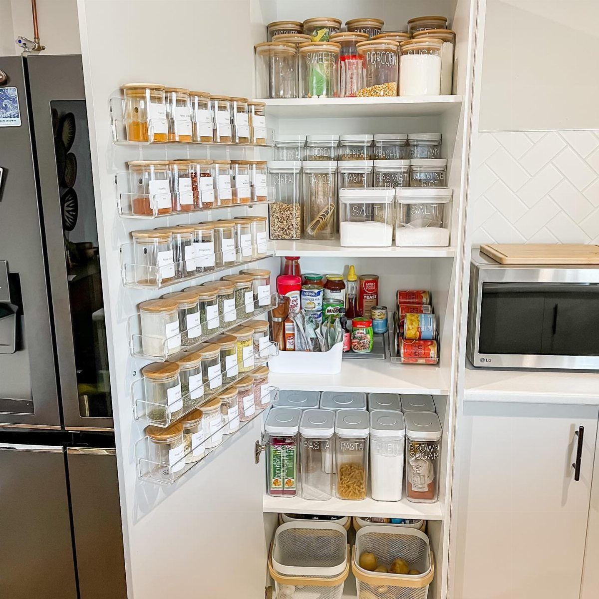 White small pantry with organized clear bins and jars containing various dry food ingredients.