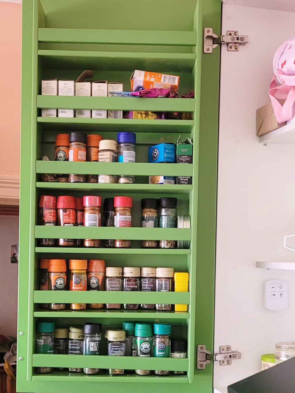26 Pull Out Drawer Kitchen Ideas That Save Space 3 Green wall cabinet with multiple shelves holding various spice jars and containers.