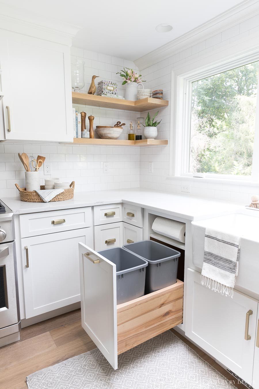 Pull-out kitchen cabinet drawer with two grey waste bins in a white kitchen.
