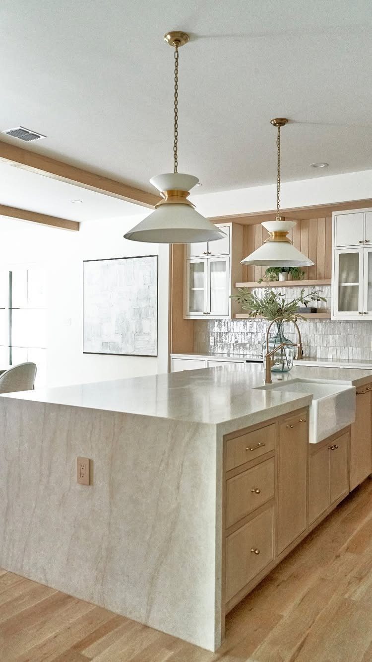 White marble waterfall island with light wood cabinets and gold pendant lighting.
