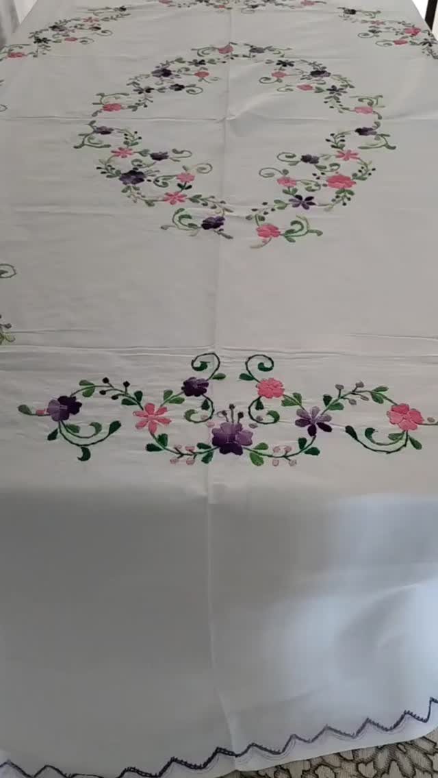 White tablecloth with purple and pink floral embroidery on a dining table.